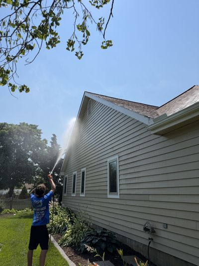 A Loukides Power Washing technician soft washing the gable end of a home