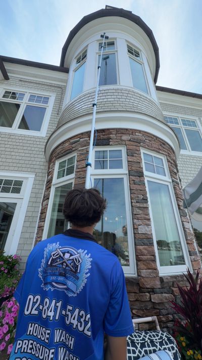 A Loukides Power Washing technician cleaning a tall bay window with a water-fed pole