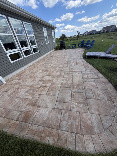 A clean curved paver patio behind a home, pond visible in the background