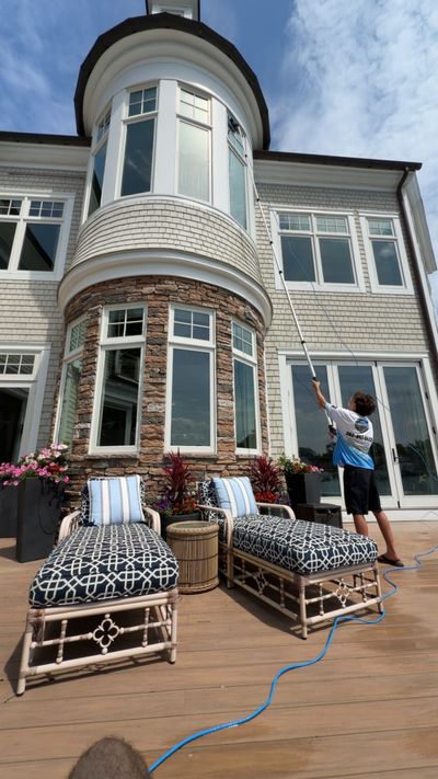 A Loukides Power Washing technician cleaning tall windows with a water-fed pole